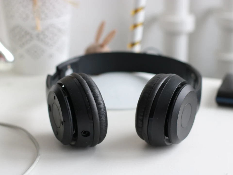 Black over-ear wireless headphones resting on a bright white desk