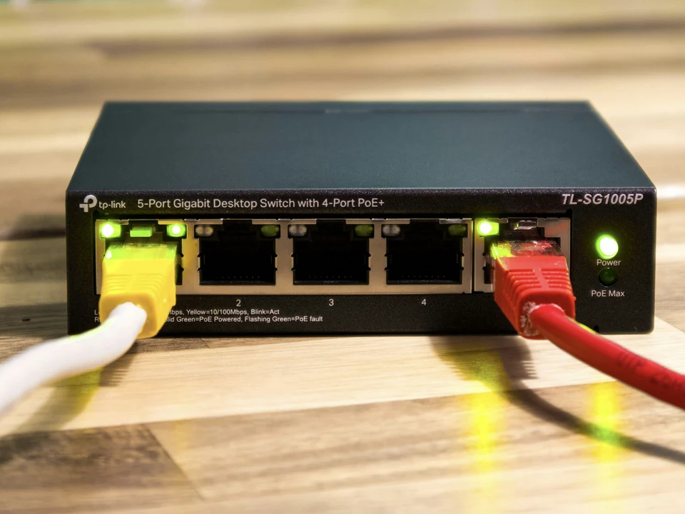 Five-port TP-Link network switch with yellow and red Ethernet cables on a wooden desk
