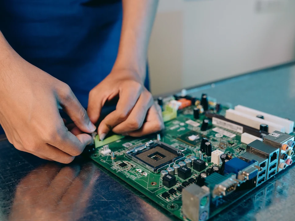 Technician's hands inspecting and working on a computer motherboard on a tidy workbench.